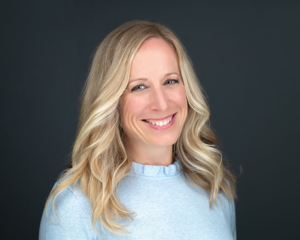 Professional headshot of a woman wearing a light blue top against a dark background